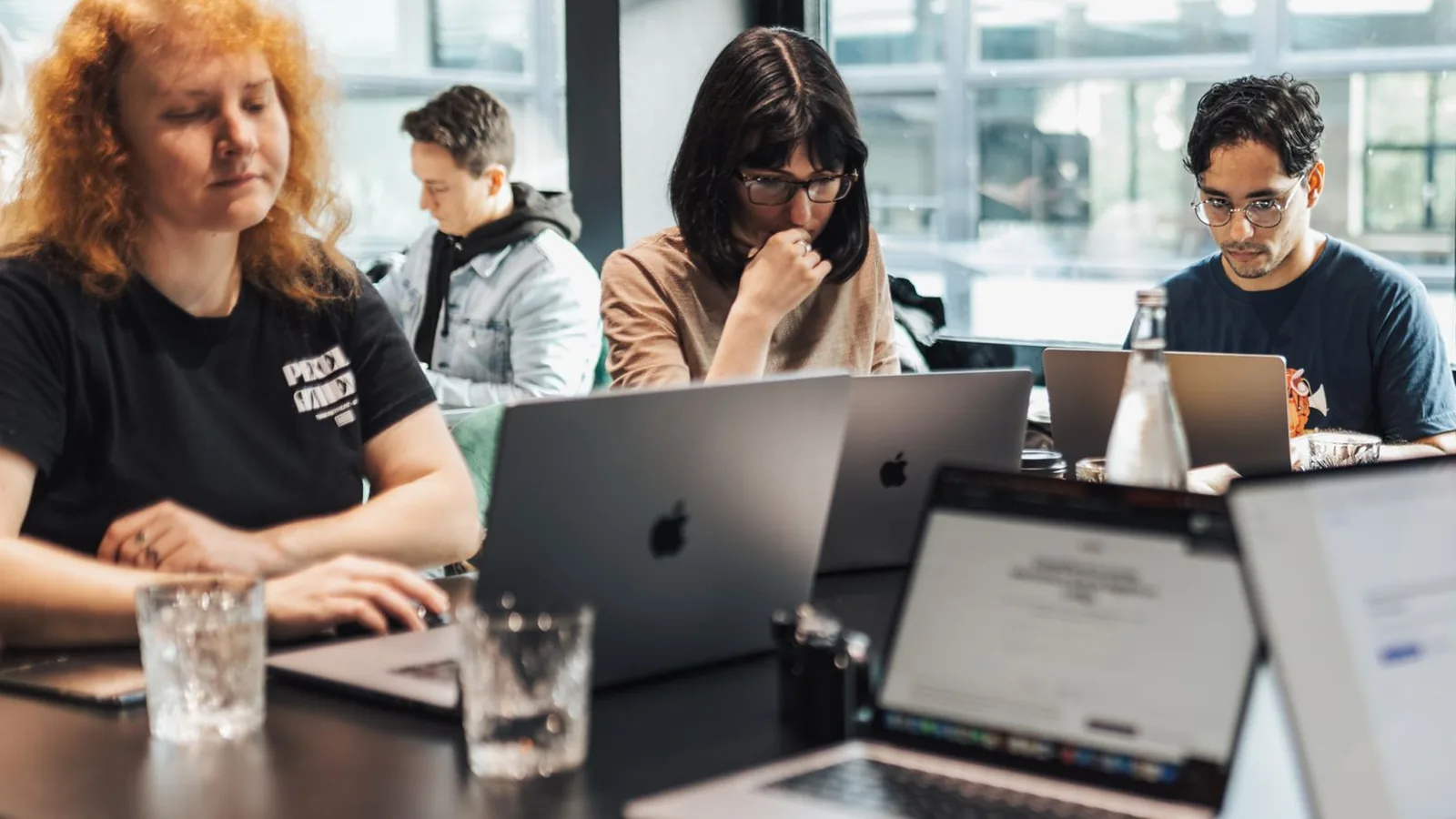Colleagues working side by side at their laptops in a bright office.