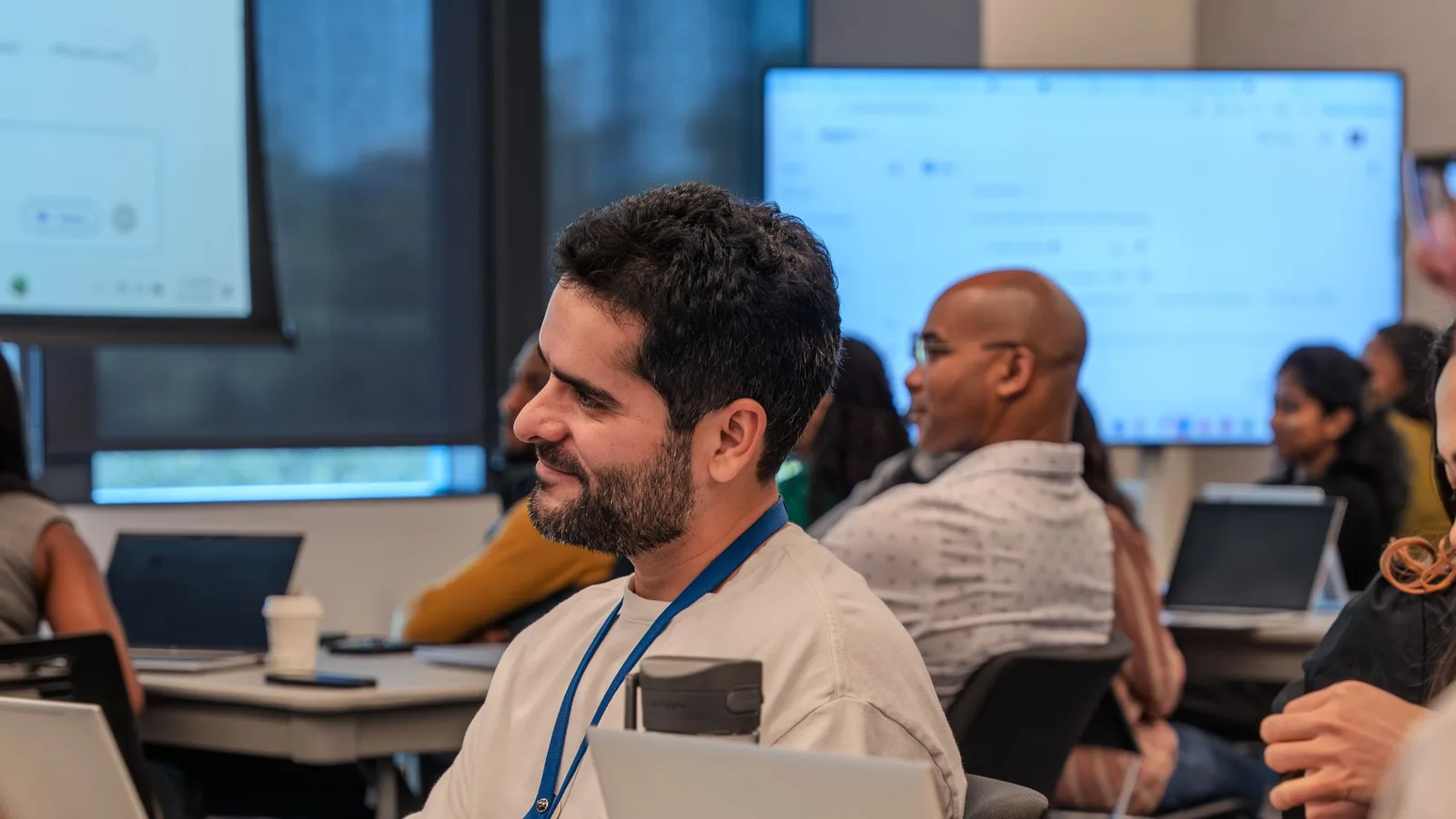 People learning at their laptops in a training session, with the work on the screen behind them.